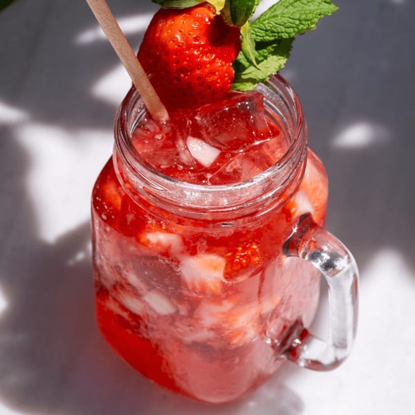 A strawberry drink in a mason jar with ice, garnished with a whole strawberry and mint.