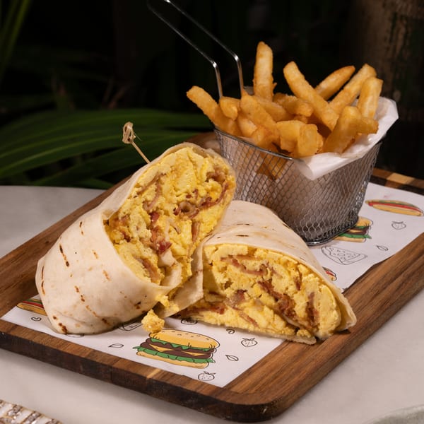 A breakfast burrito, cut in half, filled with scrambled eggs and bacon, served with fries.