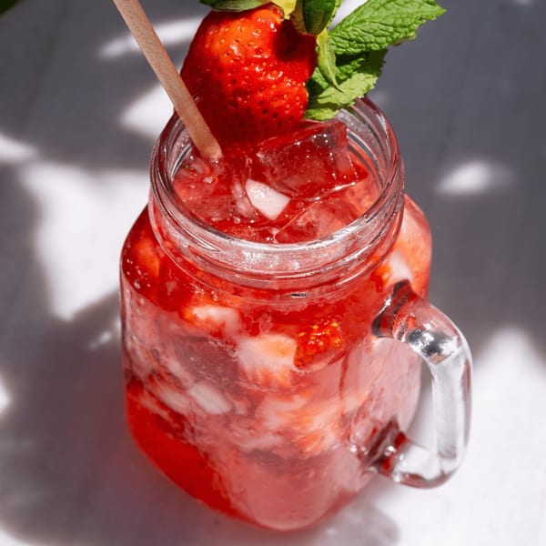 A refreshing strawberry drink in a mason jar, garnished with a whole strawberry and mint.