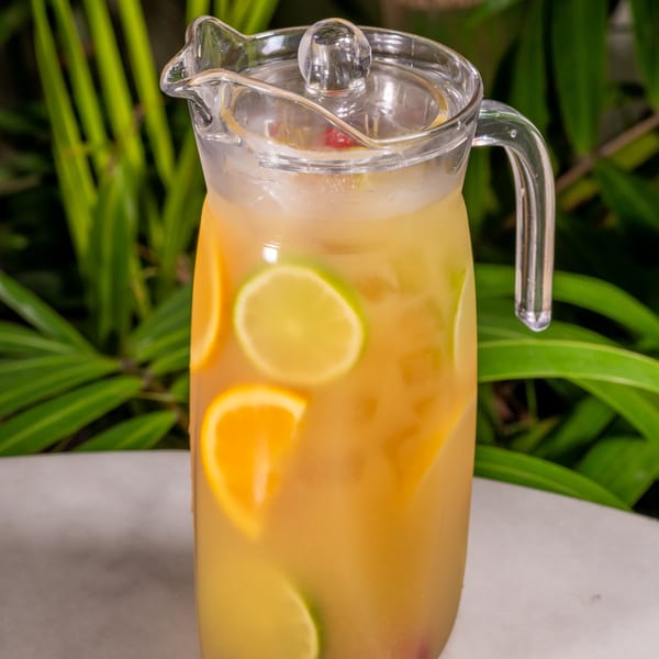 A glass pitcher of citrus-infused iced tea or punch with orange and lime slices.